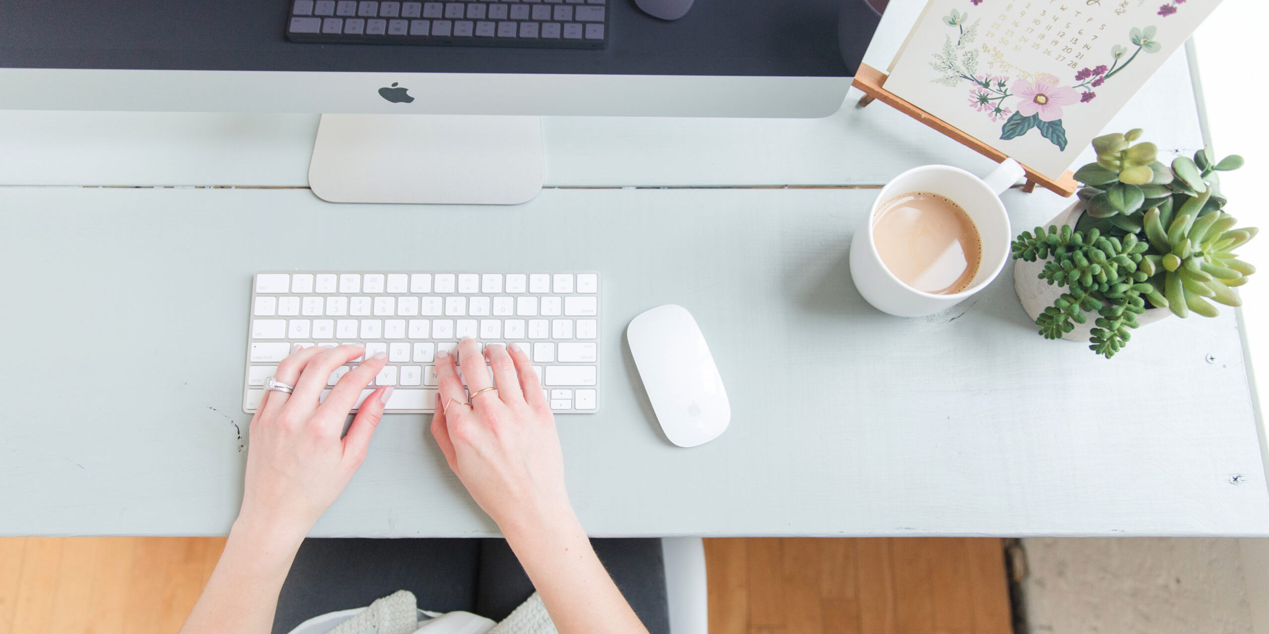 woman's hands typing on a keyboard in front of desktop computer on a pretty desk